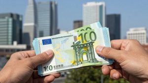 Mână cu bani europeni, clădire modernă în fundal.